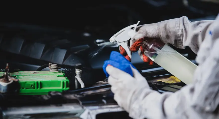 Gants et chiffon bleu pour comment nettoyer un moteur de voiture plein d'huile. Vaporisation d'un produit sur le moteur.