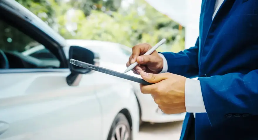 Un homme en costume bleu utilise une tablette pour évaluer la valeur vénale d'un véhicule blanc.