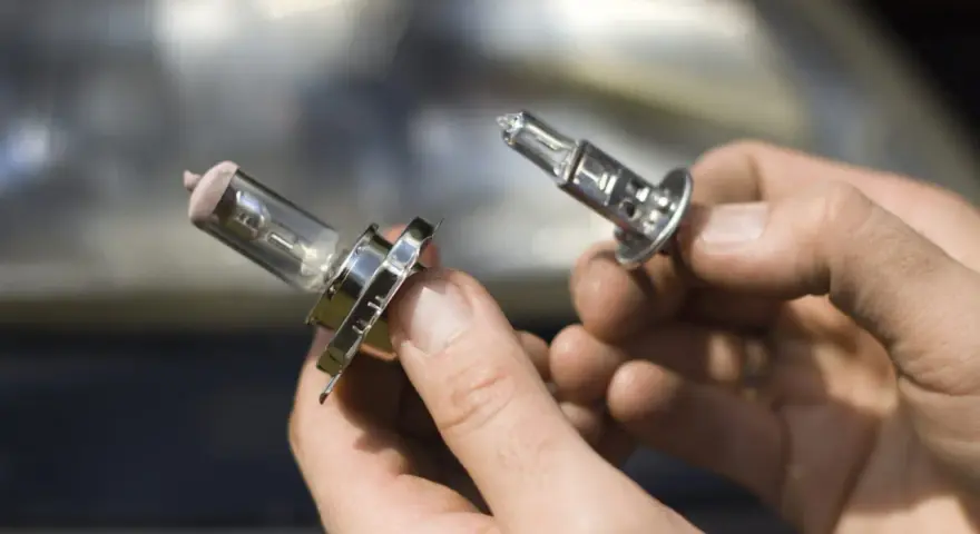 Deux ampoules de feu de croisement voiture sont tenues dans des mains. L'une est déjà retirée, l'autre est sur le point de l'être.