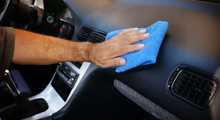 Main d'homme nettoyant le tableau de bord d'une voiture avec un chiffon bleu. Un nettoyant plastique voiture fait maison pour un intérieur impeccable.