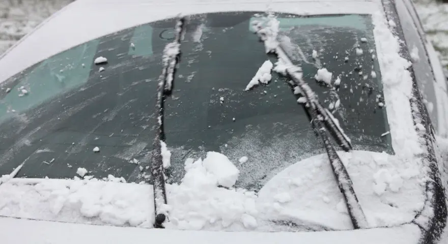 Pare-brise enneigé, un essuie-glace bloqué au milieu, prêt à dégager la vue.