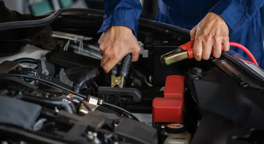 Mains de mécanicien effectuant le branchement batterie voiture avec des câbles de démarrage.