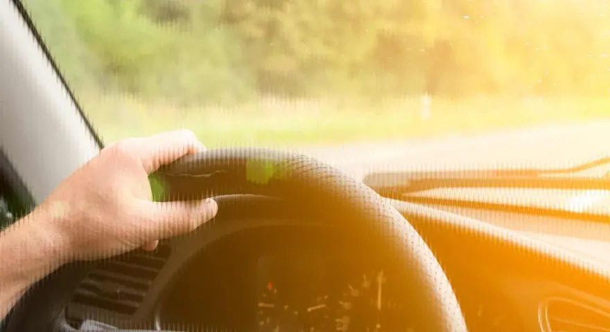 Main d'un conducteur tenant le volant d'une voiture qui tremble au point mort, sous un soleil éclatant.