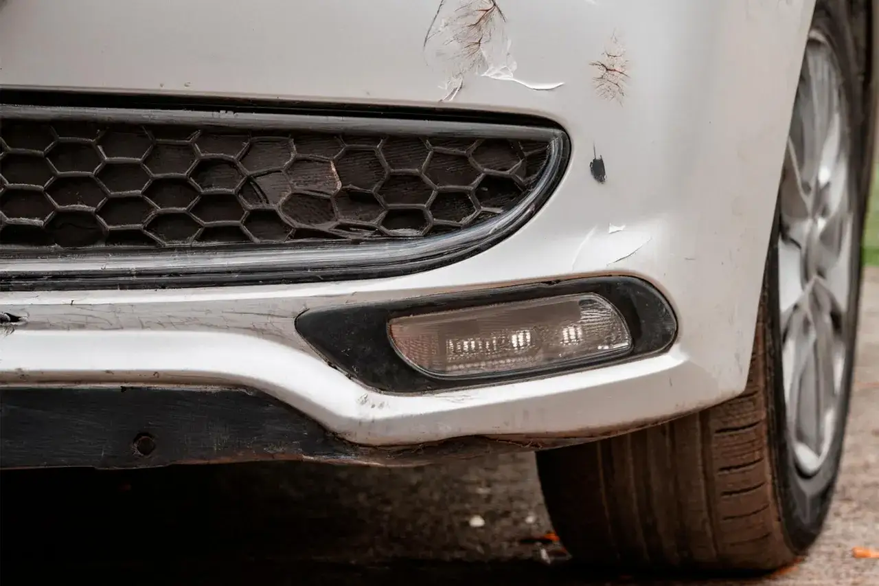 Pare-chocs avant d'une voiture blanche ab&icirc;m&eacute;. Des &eacute;clats de peinture r&eacute;v&egrave;lent la sous-couche. Une m&eacute;thode pour redresser carrosserie eau chaude pourrait aider.