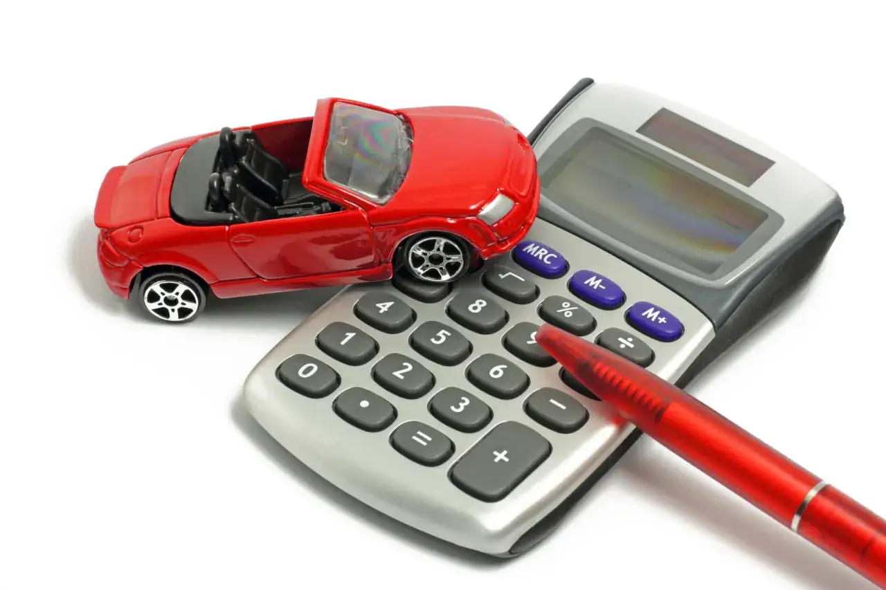 Une voiture rouge miniature sur une calculatrice, avec un stylo rouge. Id&eacute;al pour une estimation voiture.