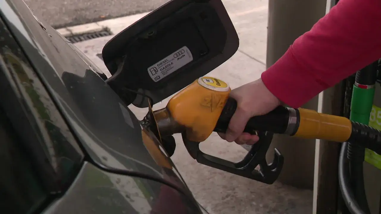 Main d'une personne tenant un pistolet de pompe à essence, le réservoir de la voiture ouvert. Attention au mauvais carburant voiture symptôme.