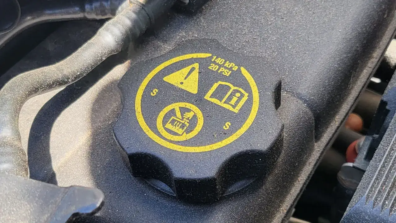 Couvercle noir avec symboles jaunes : attention, livre ouvert, et interdiction d'ouvrir à chaud. Indique la pression du liquide de refroidissement.