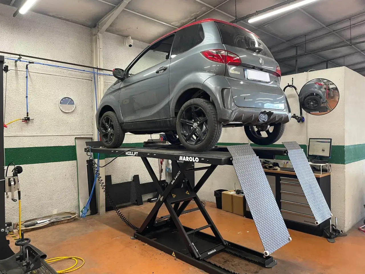 Une voiture sans permis grise sur un pont élévateur, prête pour son contrôle technique.