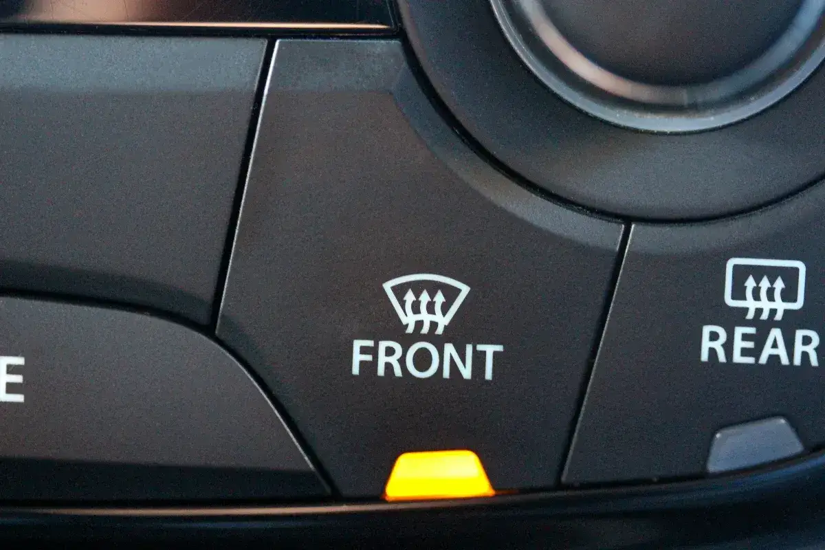 Bouton de commande de désembuage avant activé, avec un voyant orange allumé.
