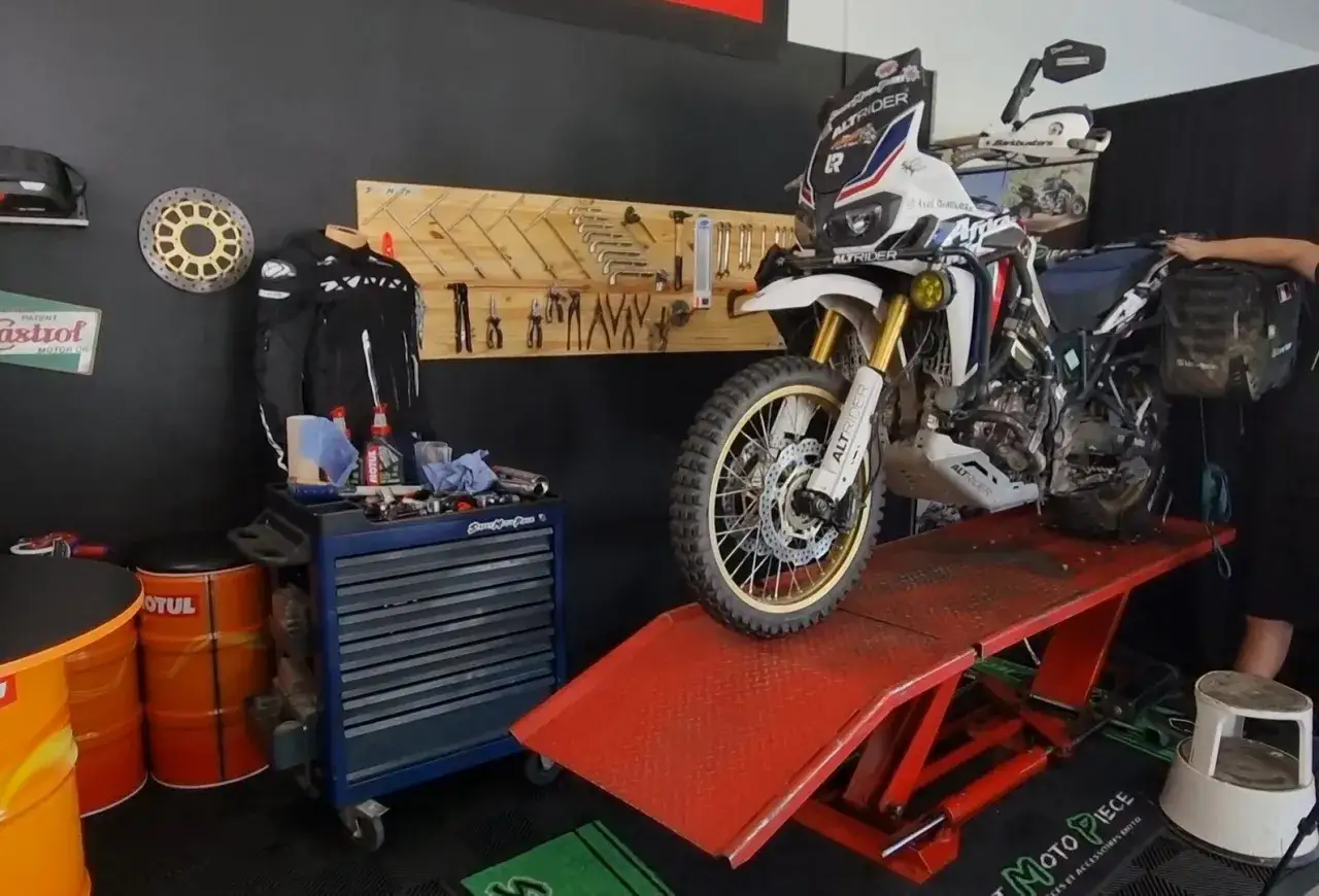 Une moto d'aventure sur un pont élévateur, prête pour un contrôle technique. Outils et équipement de moto visibles.