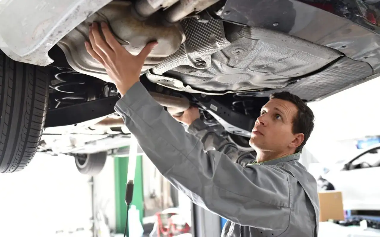 M&eacute;canicien inspectant le dessous d'une voiture, peut-&ecirc;tre pour savoir comment nettoyer un pot catalytique.
