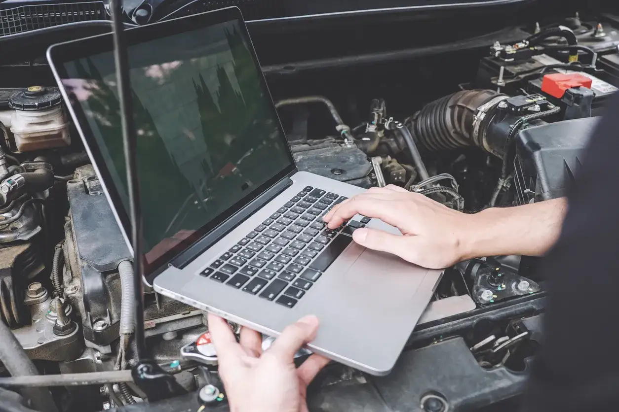 M&eacute;canicien utilisant un ordinateur portable pour r&eacute;initialiser direction assist&eacute;e &eacute;lectrique dans un compartiment moteur.