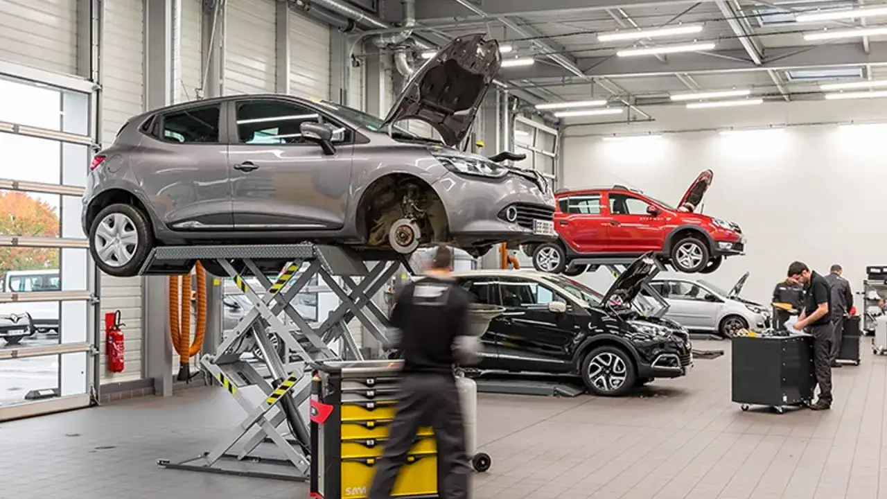 Dans un garage, plusieurs voitures sont sur des ponts &eacute;l&eacute;vateurs pour leur premi&egrave;re r&eacute;vision. Des m&eacute;caniciens s'affairent autour des v&eacute;hicules.