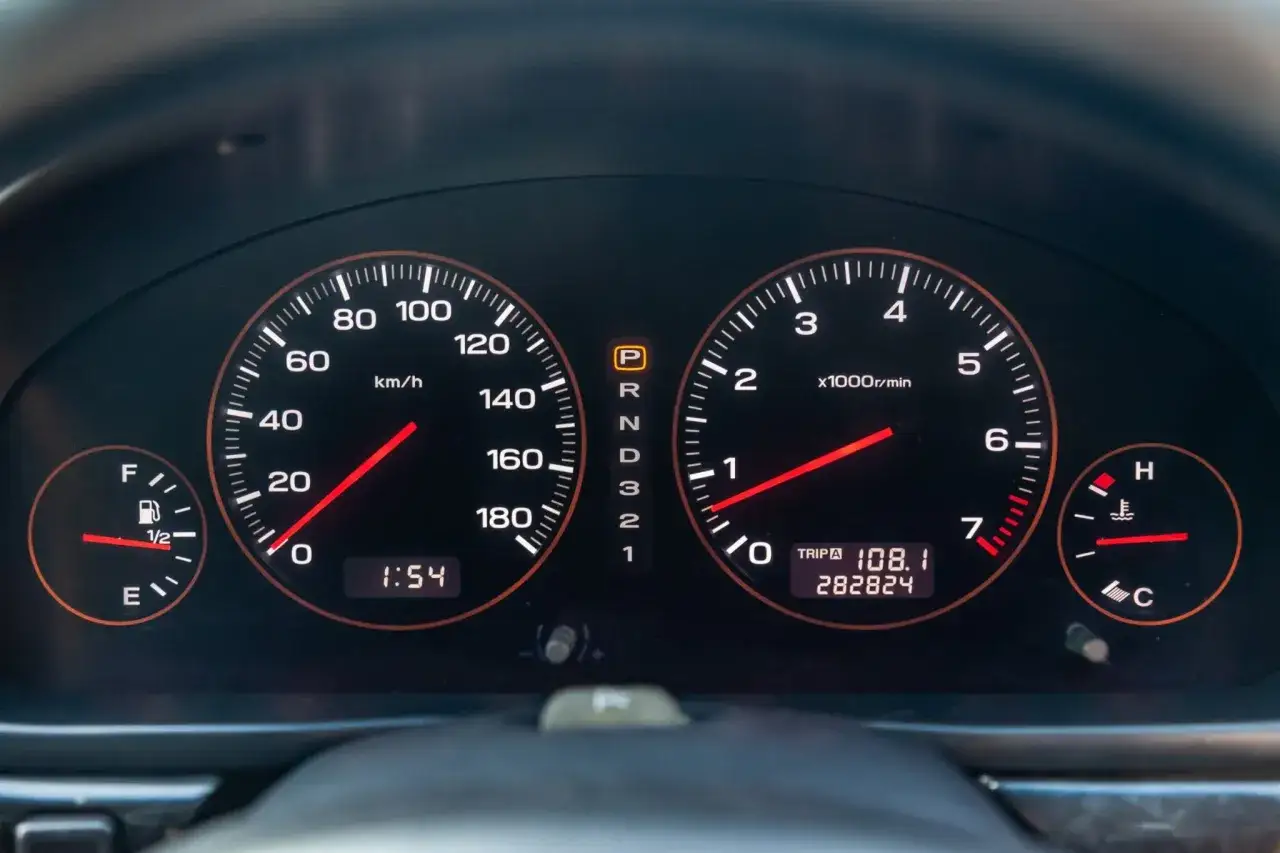 Tableau de bord d'une voiture : compteur de vitesse à 0 km/h, compte-tours à 1000 tr/min, jauge d'essence et de température. Le kilométrage total est de 282 824 km.