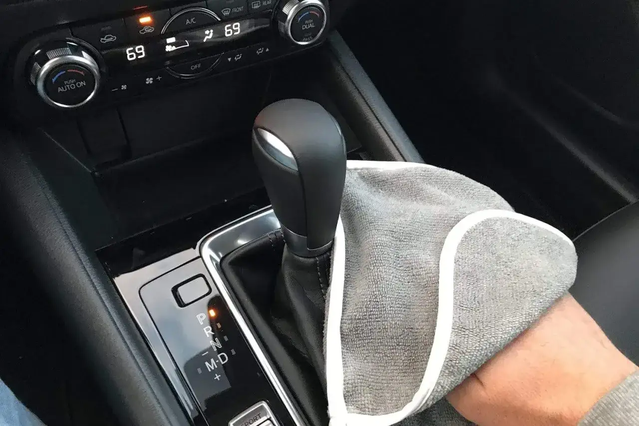 Nettoyant plastique voiture fait maison : une main tient un chiffon pour nettoyer le levier de vitesse et la console centrale.