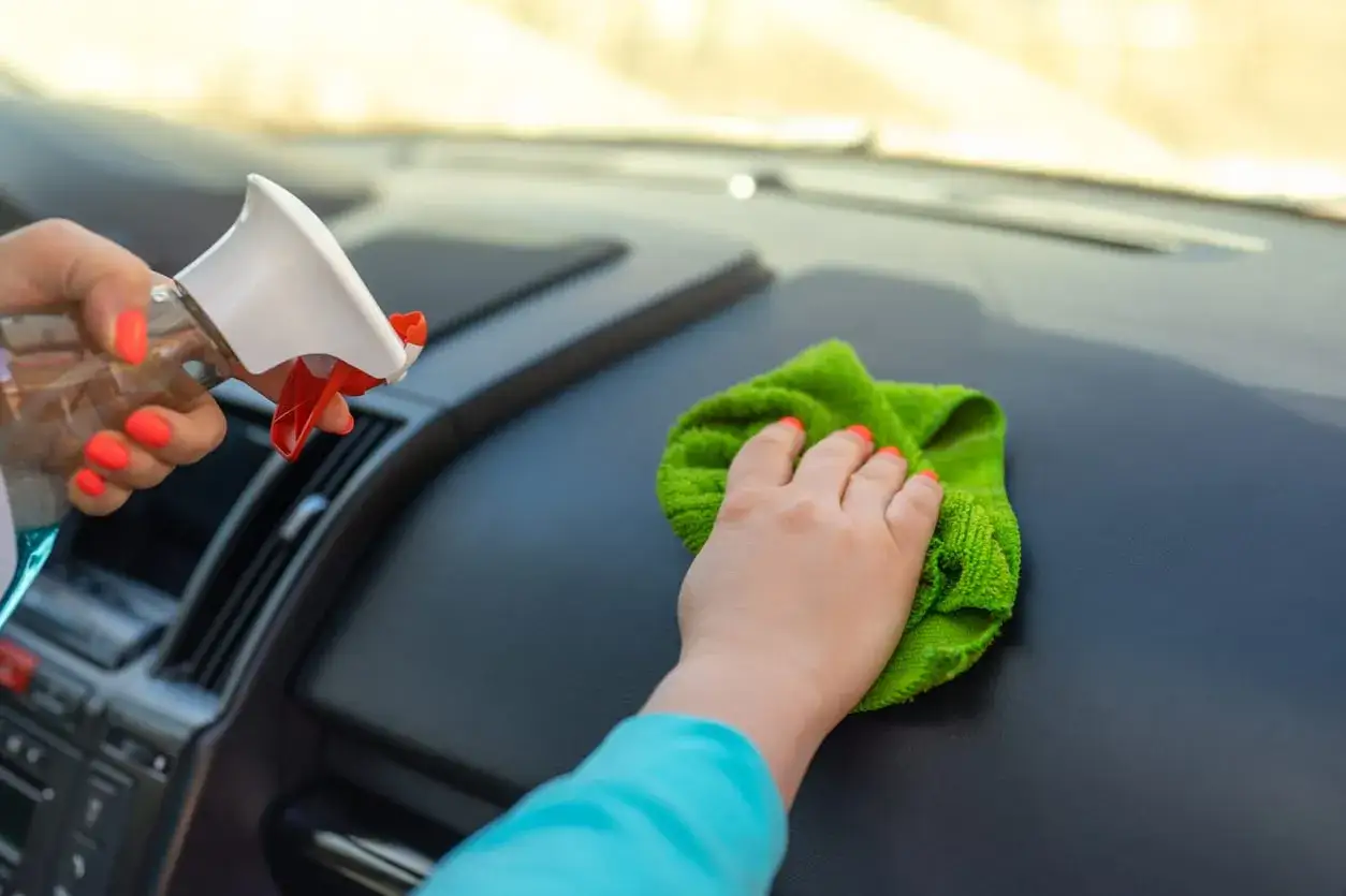 Une astuce de grand-m&egrave;re pour faire briller une voiture : nettoyage du tableau de bord avec un spray et un chiffon vert.