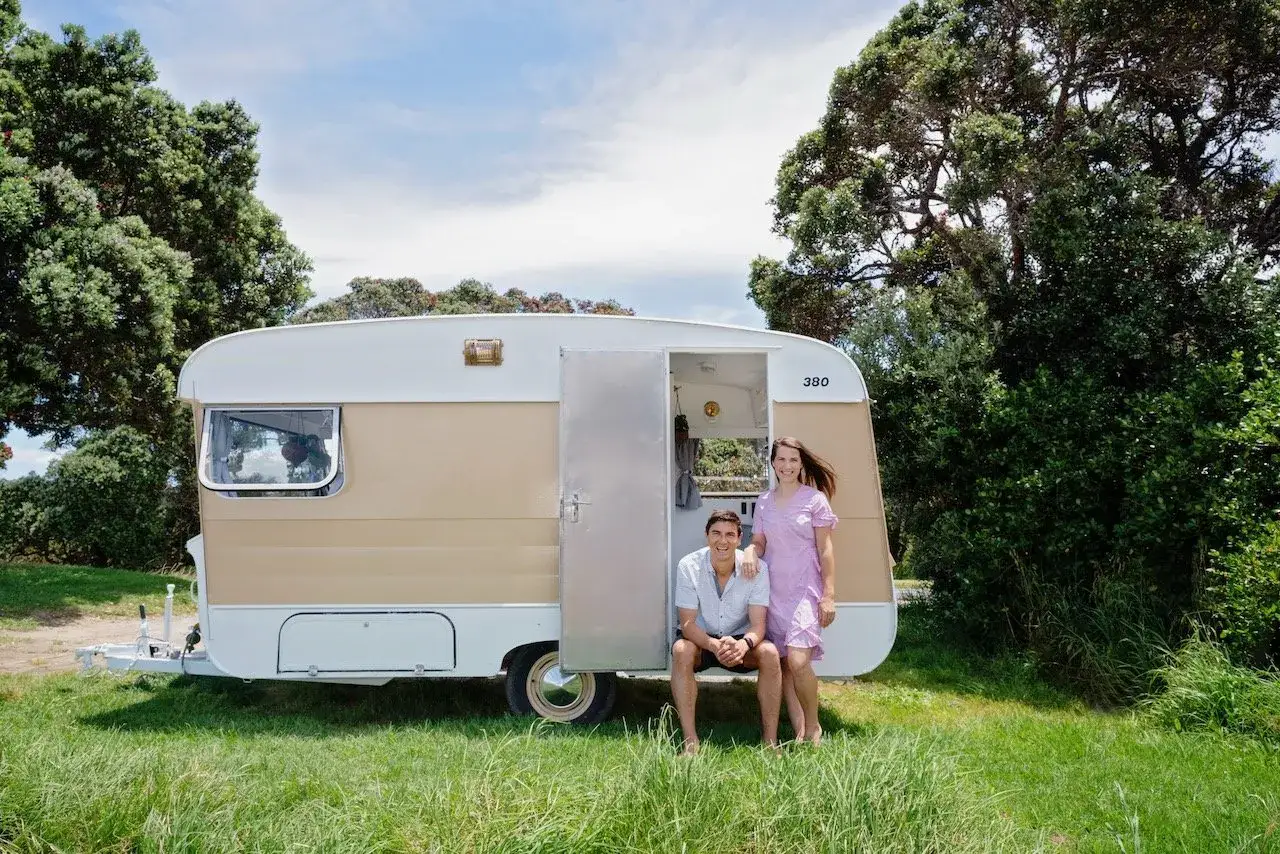 Couple pose devant leur caravane vintage, r&eacute;sultat d'une belle restauration.