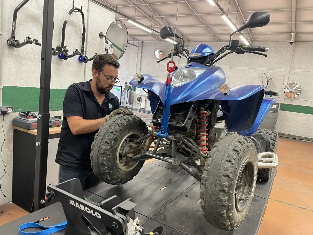 Un mécanicien effectue le contrôle technique d'un quad bleu dans un atelier.